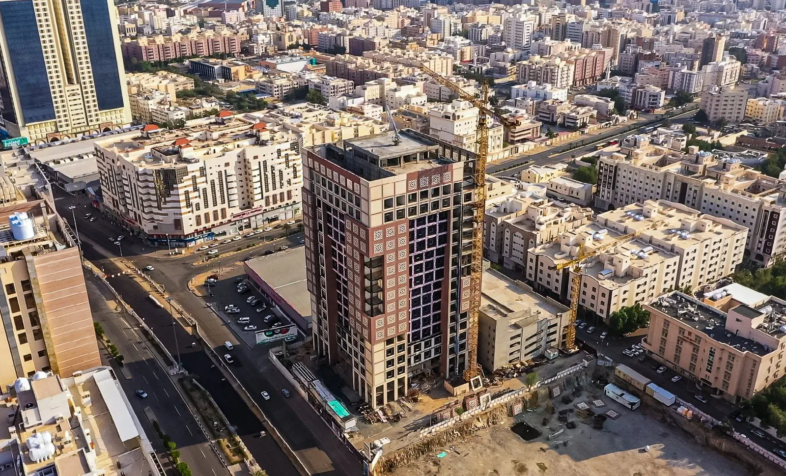 An Al Imdad high-rise tower under construction with a tower crane, above the Makkah skyline.