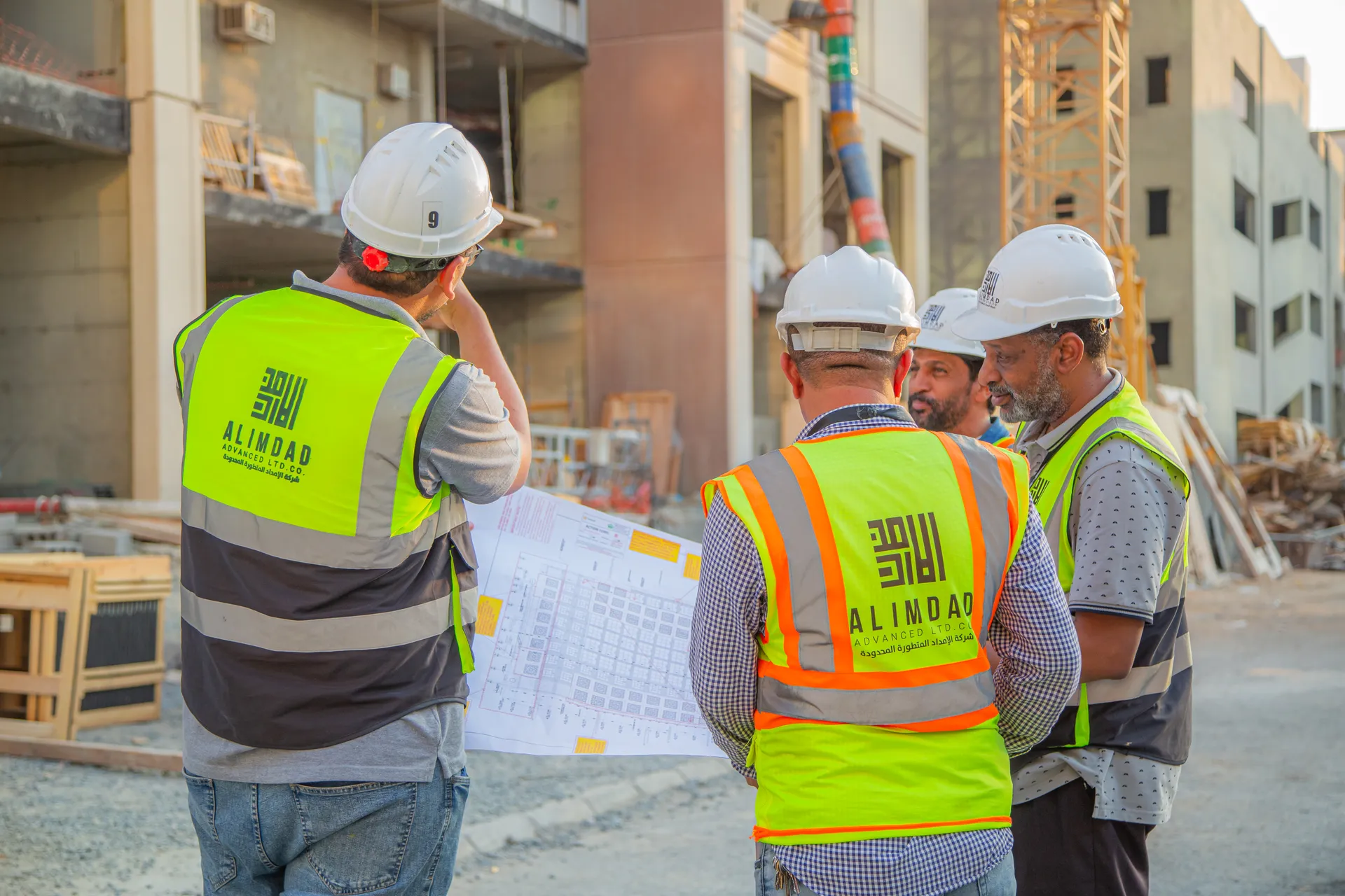 Al Imdad site team in hi-vis vests and hard hats reviewing project drawings on site.